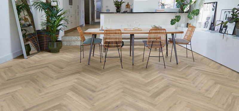 Light oak herringbone wood flooring in a modern dining room setting with a wooden dining table and woven-back chairs.